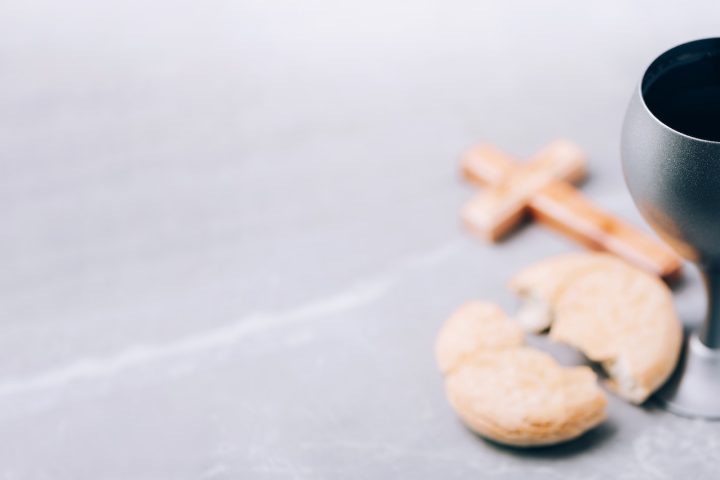 Unleavened bread, chalice of wine, wooden cross on grey background. Christian communion for reminder