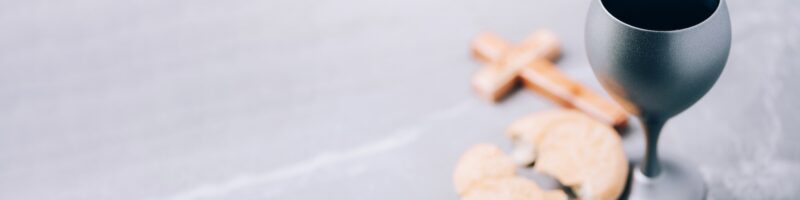 Unleavened bread, chalice of wine, wooden cross on grey background. Christian communion for reminder