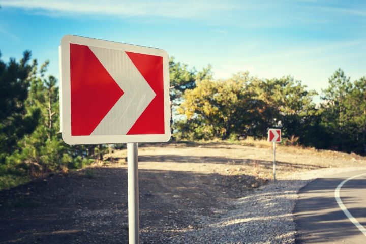 Asphalt road in autumn forest at sunrise and road sign