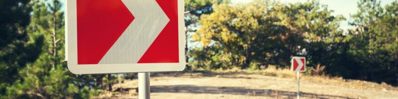 Asphalt road in autumn forest at sunrise and road sign