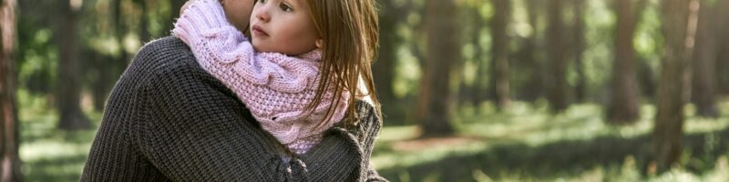 Little girl huggs her father in forest