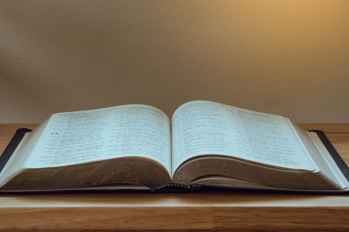 Open Bible on a wood table with light from window.
